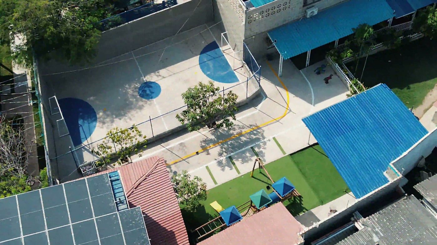 Vista aérea del campus del Gimnasio Campestre: cancha multideportiva, parque infantil con grama sintética y zonas cubiertas